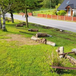FIRMA USŁUGOWA PAWEŁ FOKSIŃSKI - Przygotowanie terenu pod budowę: usunięte fragmenty betonowego ogrodzenia z wystającymi metalowymi elementami leżą na trawie wzdłuż drogi, w tle dom jednorodzinny i traktor.