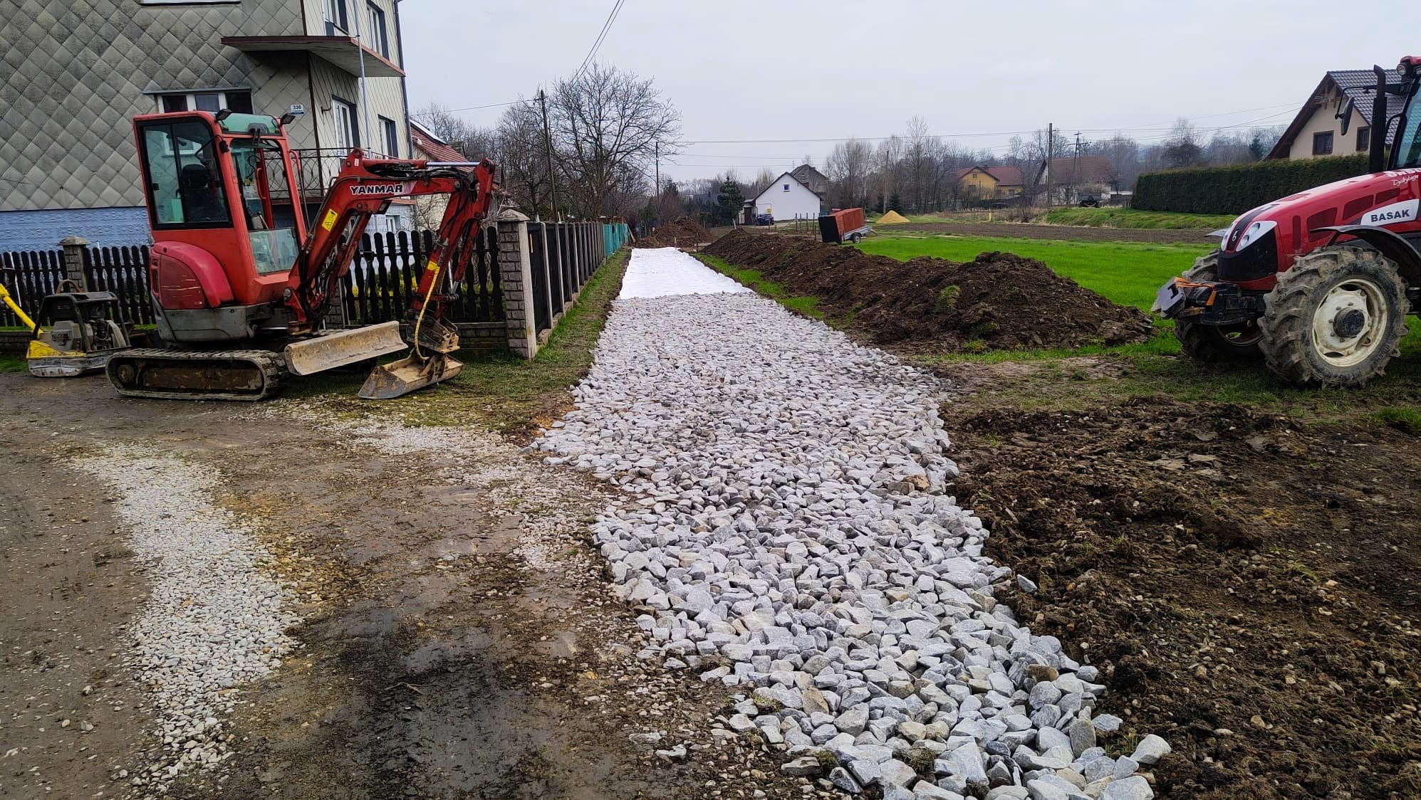 Budowa drogi dojazdowej: warstwa tłucznia na geowłókninie, widoczny minikoparka Yanmar i traktor Basak