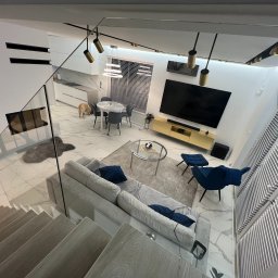 KONSTRUKTOR WM SPÓŁKA Z OGRANICZONĄ ODPOWIEDZIALNOŚCIĄ - Nowoczesny salon z marmurową podłogą, szarym narożnikiem i niebieskimi akcentami. Widok z góry na jasne wnętrze z elementami drewna i szkła, pies w tle.