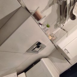 KONSTRUKTOR WM SPÓŁKA Z OGRANICZONĄ ODPOWIEDZIALNOŚCIĄ - Nowoczesna łazienka z białymi płytkami, chromowanymi detalami i minimalistycznym wyposażeniem. Uwagę przyciąga podwieszana toaleta i grzejnik drabinkowy.