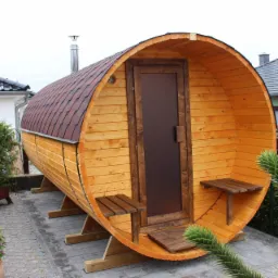 Drewniana sauna w kształcie beczki z brązowym dachem z gontu bitumicznego, umieszczona na kostce brukowej w ogrodzie, z małymi ławeczkami po bokach wejścia i metalowym kominem.