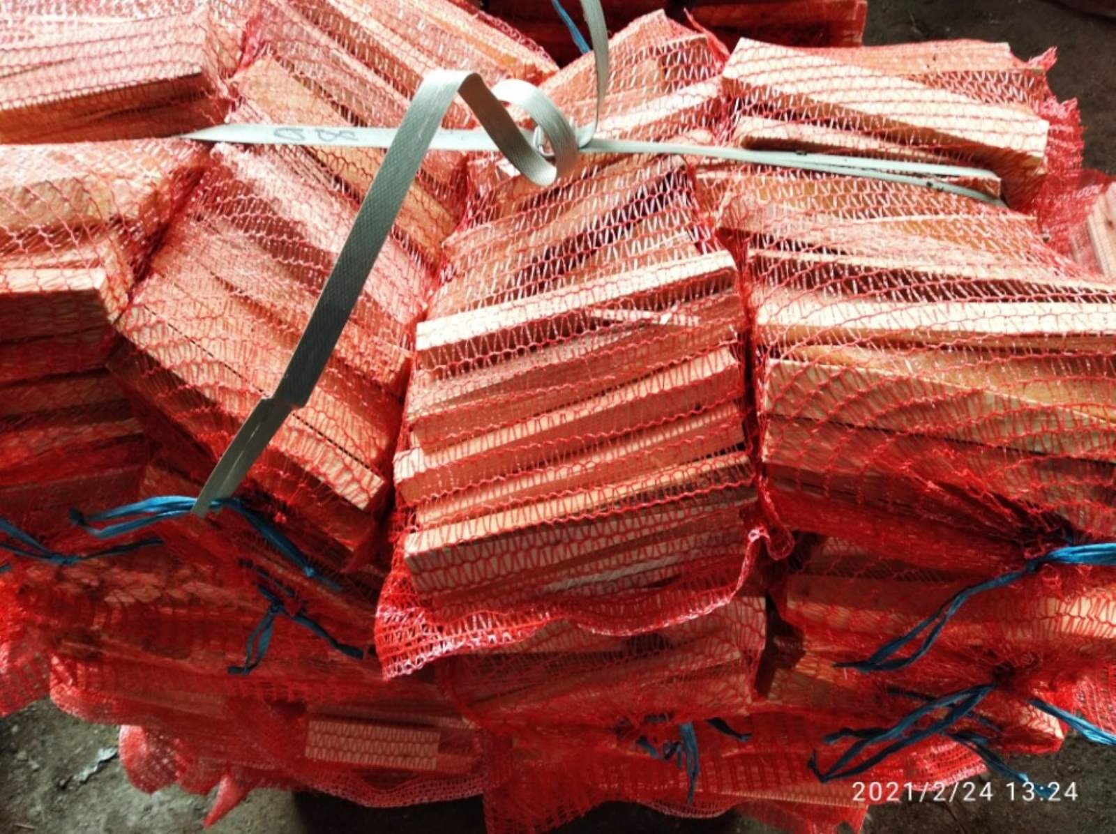 Stos worków z pociętym drewnem kominkowym, zabezpieczonych czerwoną siatką i spiętych szarą taśmą.