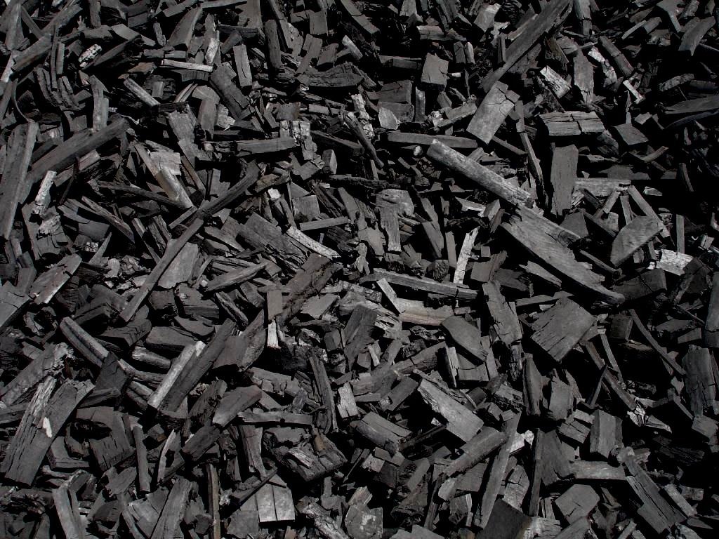 Góra czarnych, nieregularnych kawałków zwęglonego drewna, prawdopodobnie brykietu drzewnego, z widoczną strukturą drewna i nierównymi krawędziami.