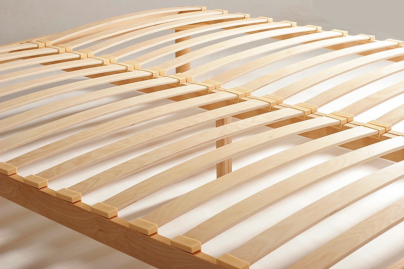 Drewniany stelaż łóżka z listew giętych, widoczny z bliska pod kątem, z jasnymi elementami łączącymi.