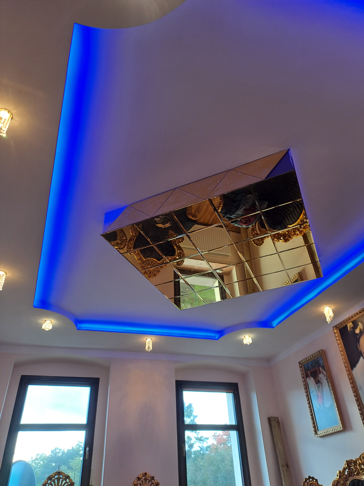 Sufit w Bierawie z podwieszaną konstrukcją i lustrzaną mozaiką w kształcie kwadratu, oświetlony niebieskim światłem LED, widok z dołu.
