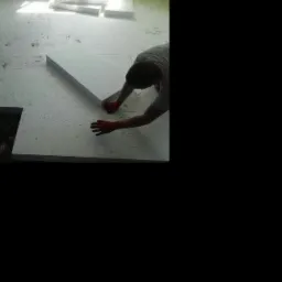 Układanie białych płyt izolacyjnych na podłodze, widoczne ręce w czerwonych rękawicach i fragment ciemnej przestrzeni w podłodze.