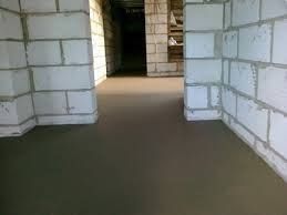 Świeżo wylana, gładka posadzka w pomieszczeniu z surowymi ścianami z białych bloczków, widoczne przejście do kolejnego pomieszczenia.