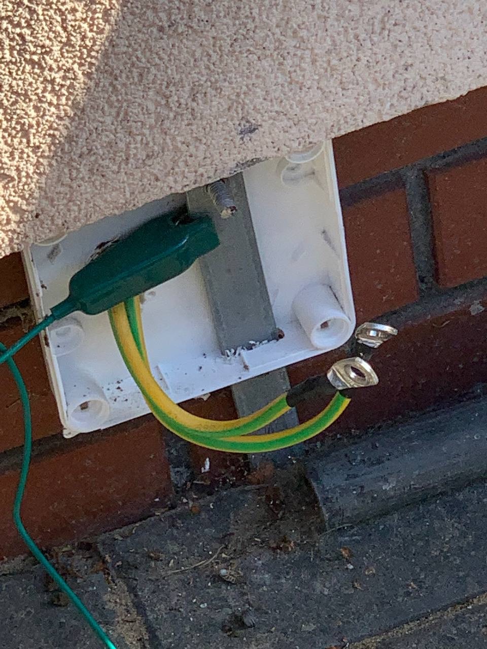 Szczegółowe ujęcie połączenia uziemiającego z kablem żółto-zielonym w puszce na ceglanej ścianie, widoczne złącza kablowe i elementy instalacji elektrycznej.