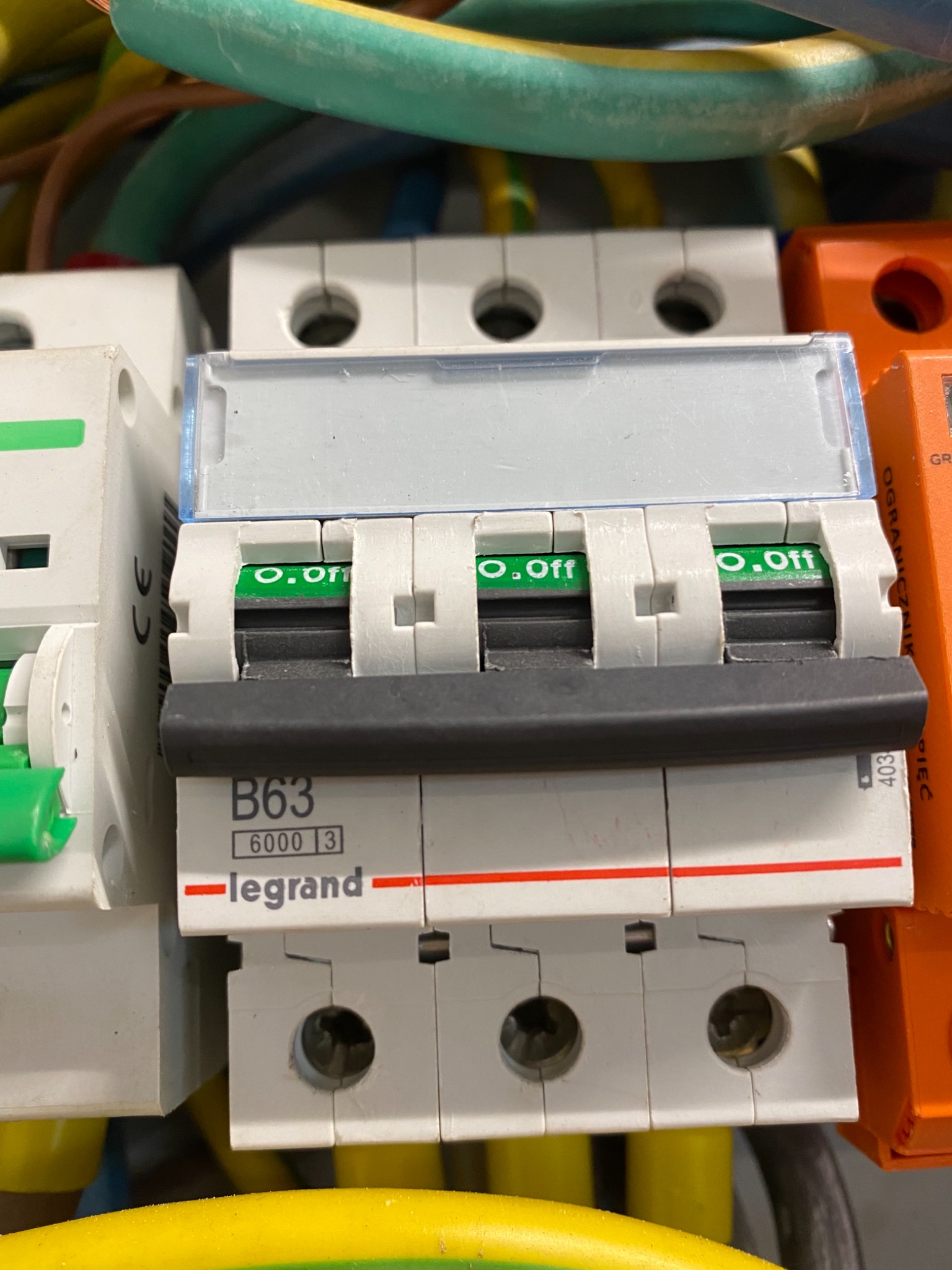 Szczegółowe zbliżenie na wyłączniki nadprądowe marki Legrand B63 w rozdzielnicy elektrycznej, widoczne przewody w różnych kolorach.