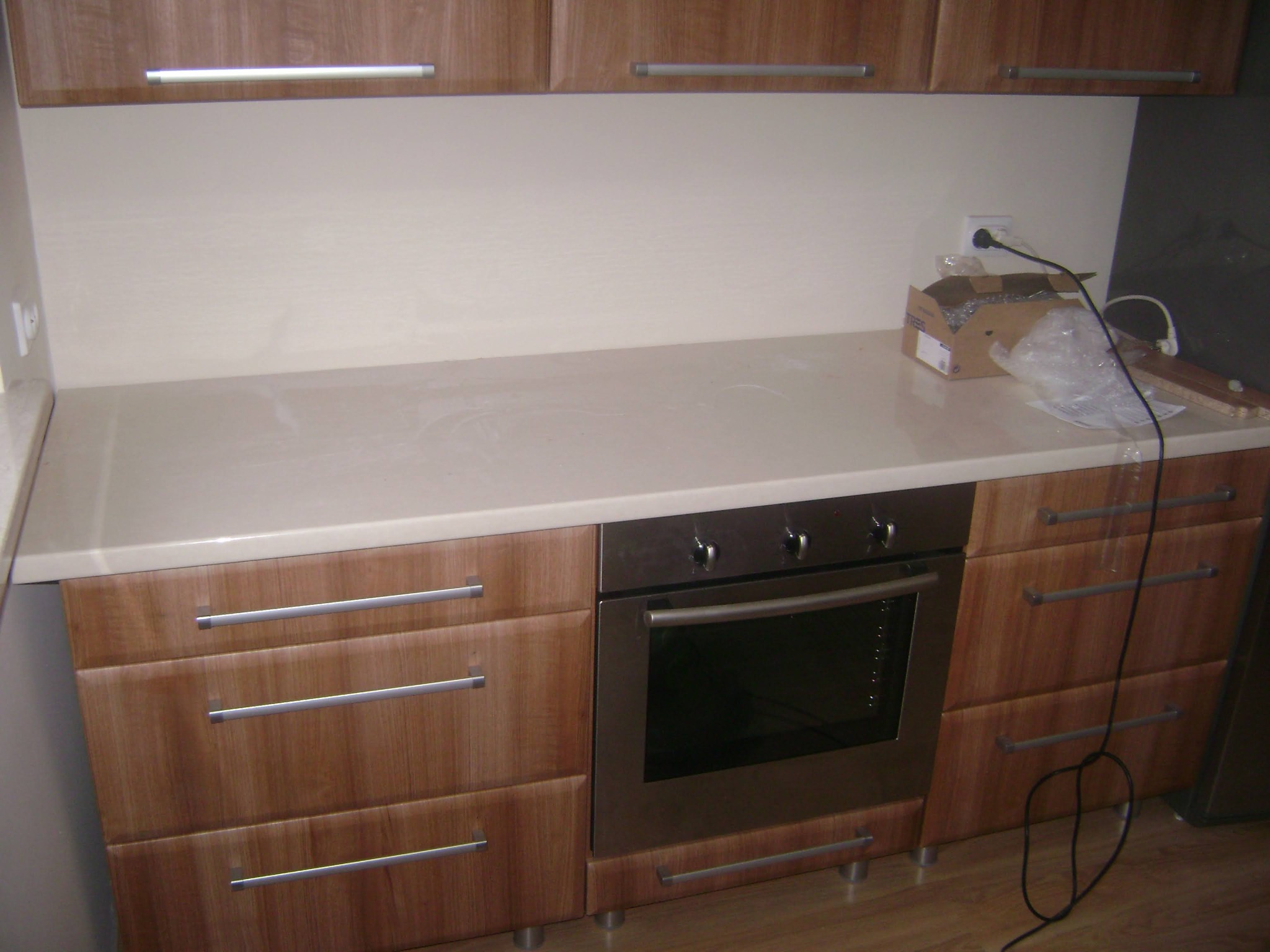 Fragment kuchni z drewnianymi szafkami z poziomymi uchwytami i wbudowanym piekarnikiem; na blacie karton po sprzęcie i przewody elektryczne