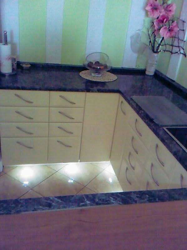 Jasna kuchnia z szufladami, ciemnym blatem i podświetleniem pod szafkami, widok z góry na narożnik.