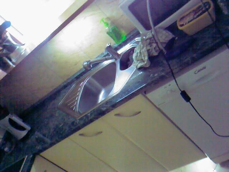 Zlewozmywak ze stali nierdzewnej wbudowany w blat z ciemnego marmuru, widoczna bateria, dozownik na płyn, ściereczka, zlewanka i częściowo widoczna zmywarka Candy.