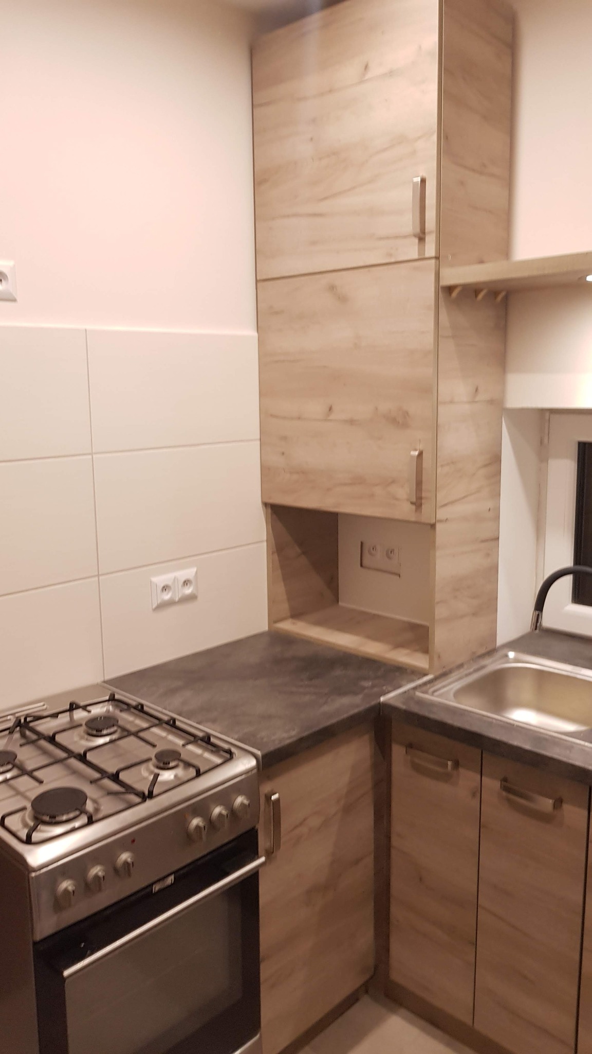 Fragment kuchni z zabudową w odcieniach drewna, płyta gazowa, zlewozmywak i białe płytki na ścianie.