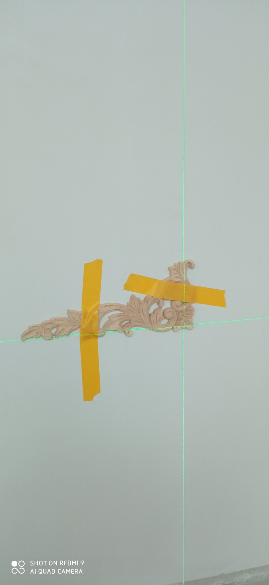 Drewniana, ozdobna listwa przymocowana do ściany za pomocą żółtej taśmy, wyznaczona linią lasera.