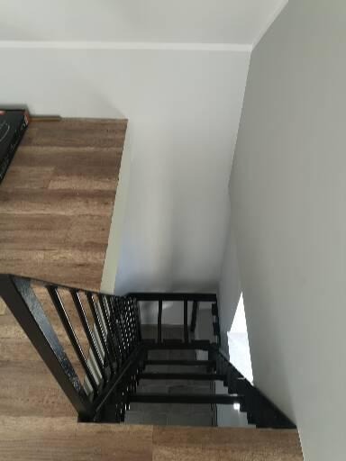 Wysoki kąt patrzenia na czarne, metalowe schody z poręczą, osadzone w jasnym wnętrzu z drewnopodobną okładziną ściany i białymi ścianami.