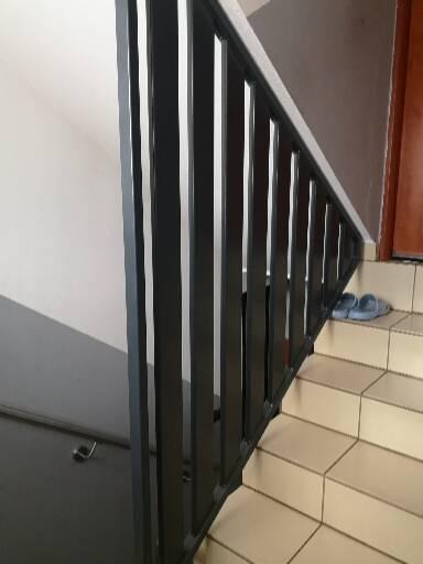 Czarne, metalowe barierki schodowe z pionowymi prętami, widoczne z bliska w Jarocinie, z parą niebieskich kapci na górnych stopniach.