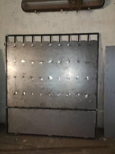 Surowa, metalowa konstrukcja z otworami, spawana z profili, stojąca na podłodze w warsztacie, oświetlona lampą jarzeniową.