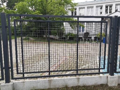 Czarne, metalowe ogrodzenie panelowe z kwadratową siatką, z dodatkową ramą wewnątrz, na tle budynku.