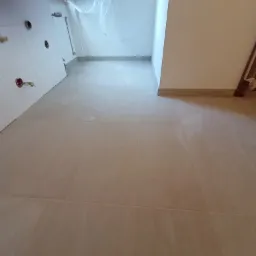 Beżowe płytki podłogowe ułożone w łazience w trakcie remontu, widoczne przygotowane ściany pod zabudowę, zabezpieczone okno folią.