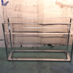 Astern - Metalowa konstrukcja regału z profili zamkniętych, spawana, w surowym stanie, na tle kartonów i narzędzi w warsztacie.