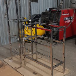 Astern - Dwie metalowe konstrukcje szkieletowe z rur, prawdopodobnie w trakcie produkcji w warsztacie, z widocznym sprzętem spawalniczym w tle.