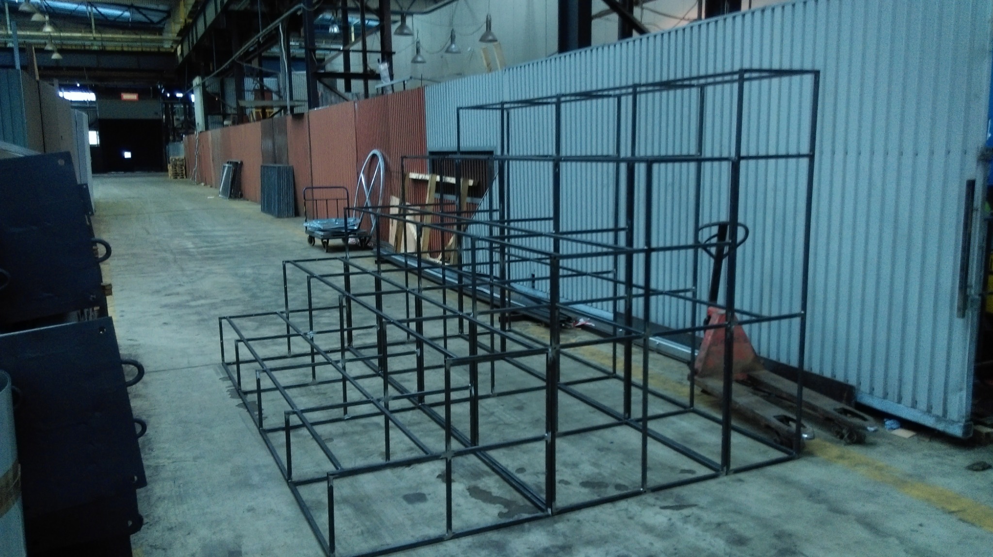 Surowa, spawana konstrukcja schodowa z metalowych profili kwadratowych, widoczna w hali produkcyjnej, obok wózek paletowy i elementy blaszane.