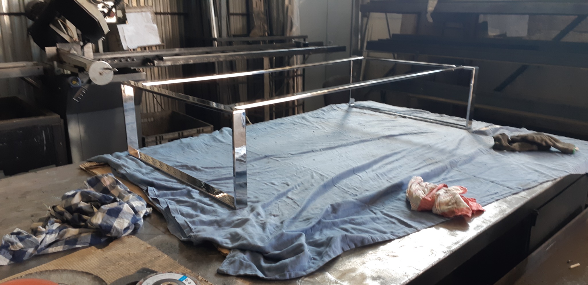 Element konstrukcji ze stali nierdzewnej w warsztacie, prawdopodobnie rama balustrady lub poręczy, leżąca na stole roboczym przykrytym płachtą.