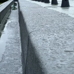 Wypełniona wodą rynna na płaskim dachu pokrytym kroplami deszczu, widoczne elementy wentylacji.