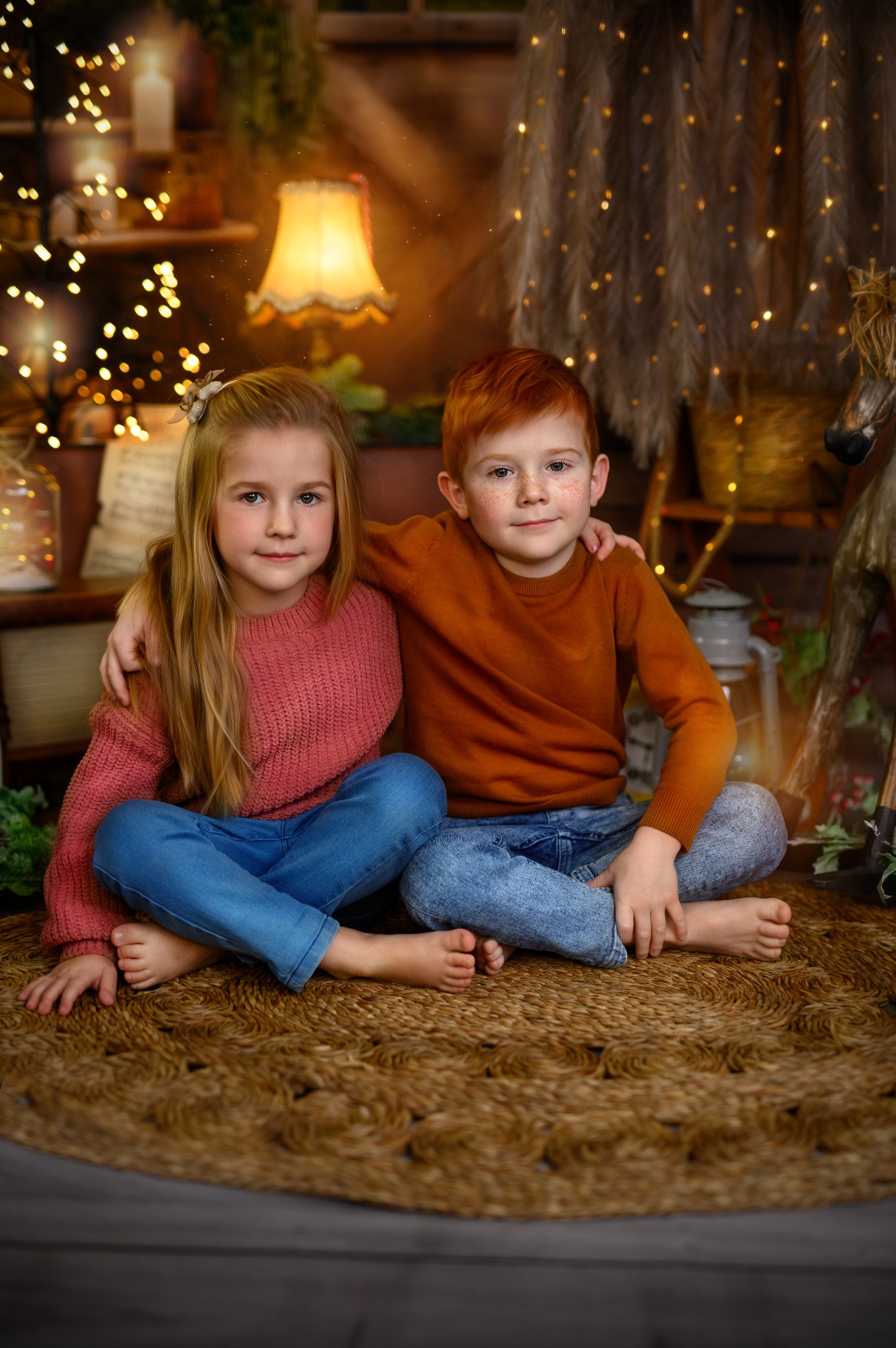 Brat i siostra siedzą na podłodze, obejmując się, w tle dekoracje z lampkami i lampą na stoliku.
