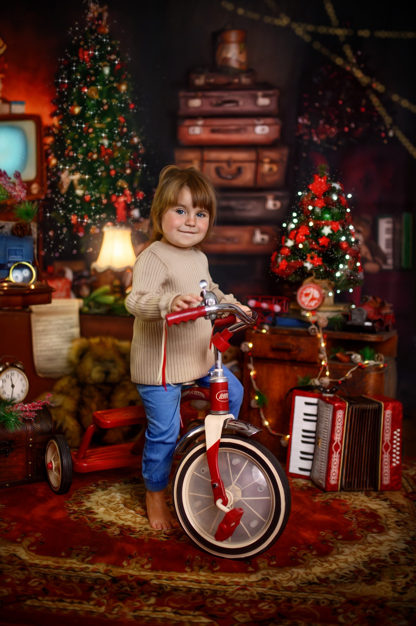 Dziewczynka na czerwonym rowerku trójkołowym w świątecznej scenerii z choinkami, starymi walizkami i akordeonem.