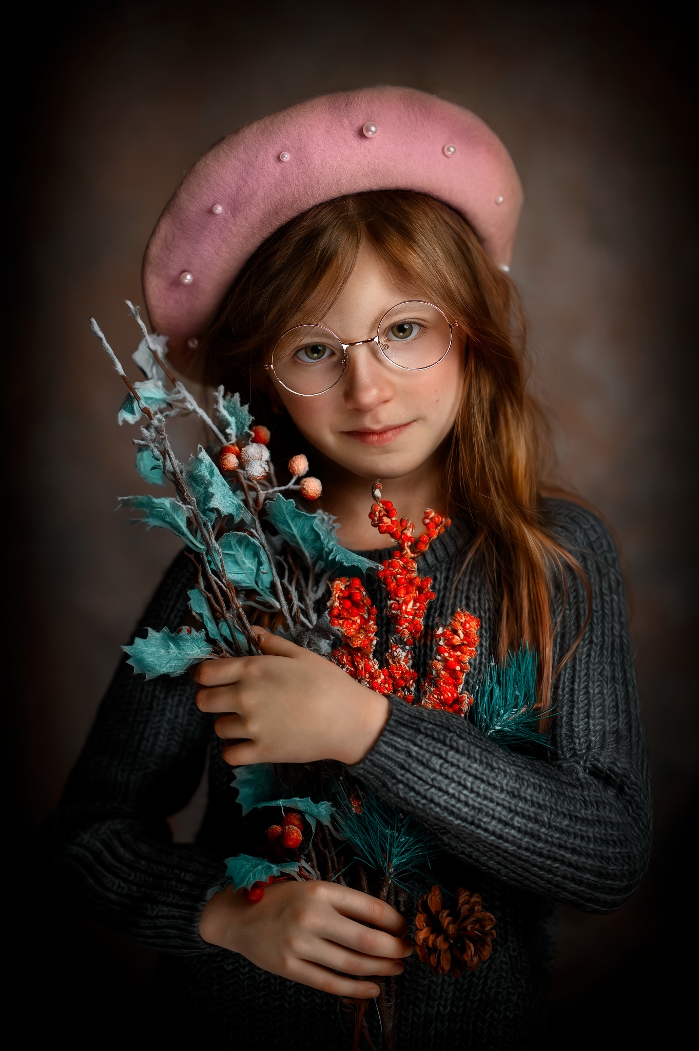 Portret dziewczynki w okularach i różowym berecie, trzymającej dekoracyjne gałązki z czerwonymi owocami i szyszką na ciemnym tle.