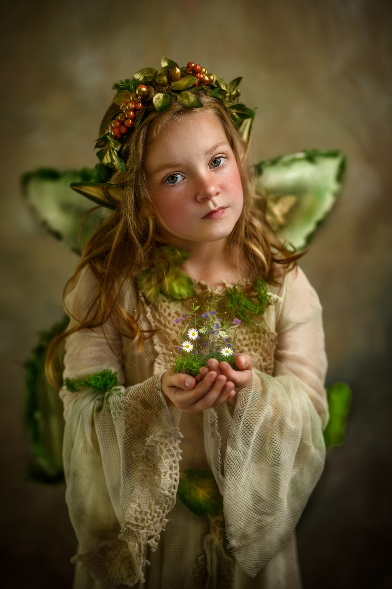 Dziewczynka w kostiumie leśnej wróżki z wiankiem na głowie i sztucznymi uszami trzymająca w dłoniach mały bukiecik polnych kwiatów.