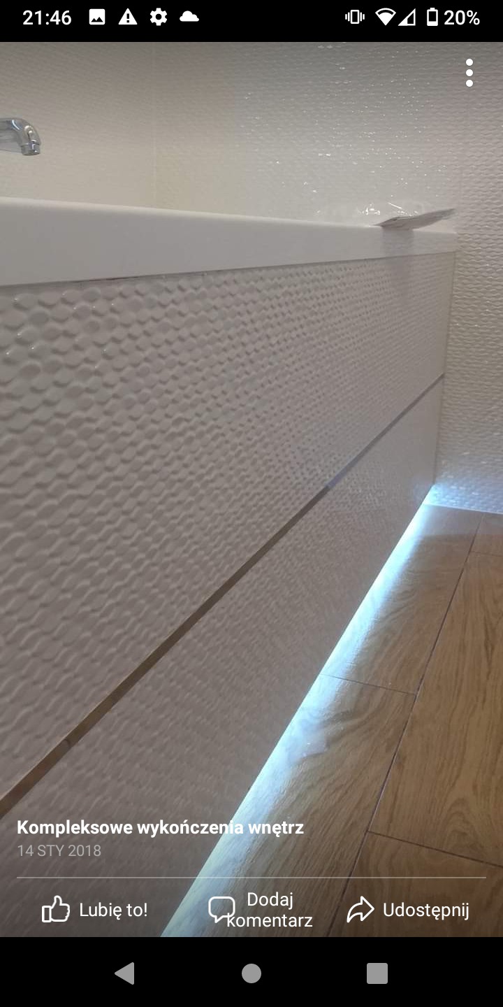 Biała szafka łazienkowa z dekoracyjną fakturą i podświetleniem LED u dołu, drewnopodobna podłoga, fragment białej ściany z teksturą w tle.