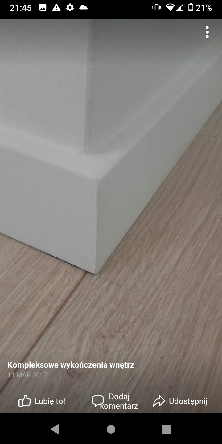 Detal wykończenia wnętrza: biała listwa przypodłogowa idealnie dopasowana do drewnianej podłogi, z precyzyjnym łączeniem narożnika ściany.