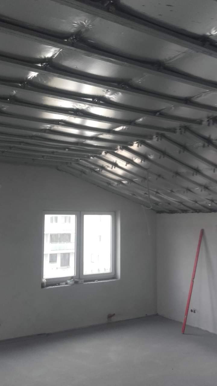 Montaż stelaża pod płytę karton gips na poddaszu, widoczna izolacja folią aluminiową, w tle okno i poziomica oparta o ścianę.