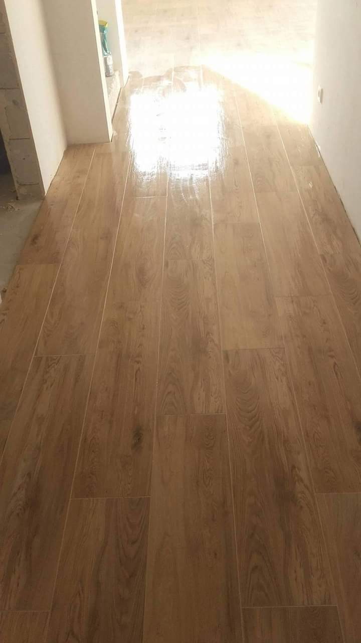 Ułożona podłoga z płytek imitujących drewno w wąskim korytarzu, widoczne fugi i odbicie światła na gładkiej powierzchni.