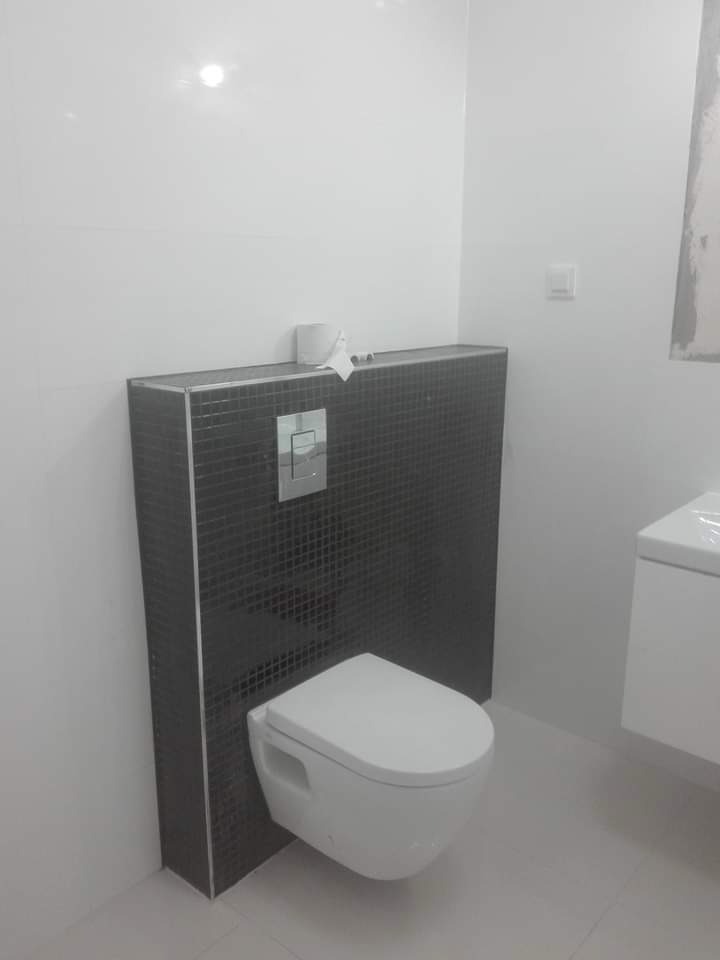 Nowoczesna, podwieszana toaleta z czarną mozaiką na stelażu, białe płytki ścienne i podłogowe, minimalistyczny design łazienki.