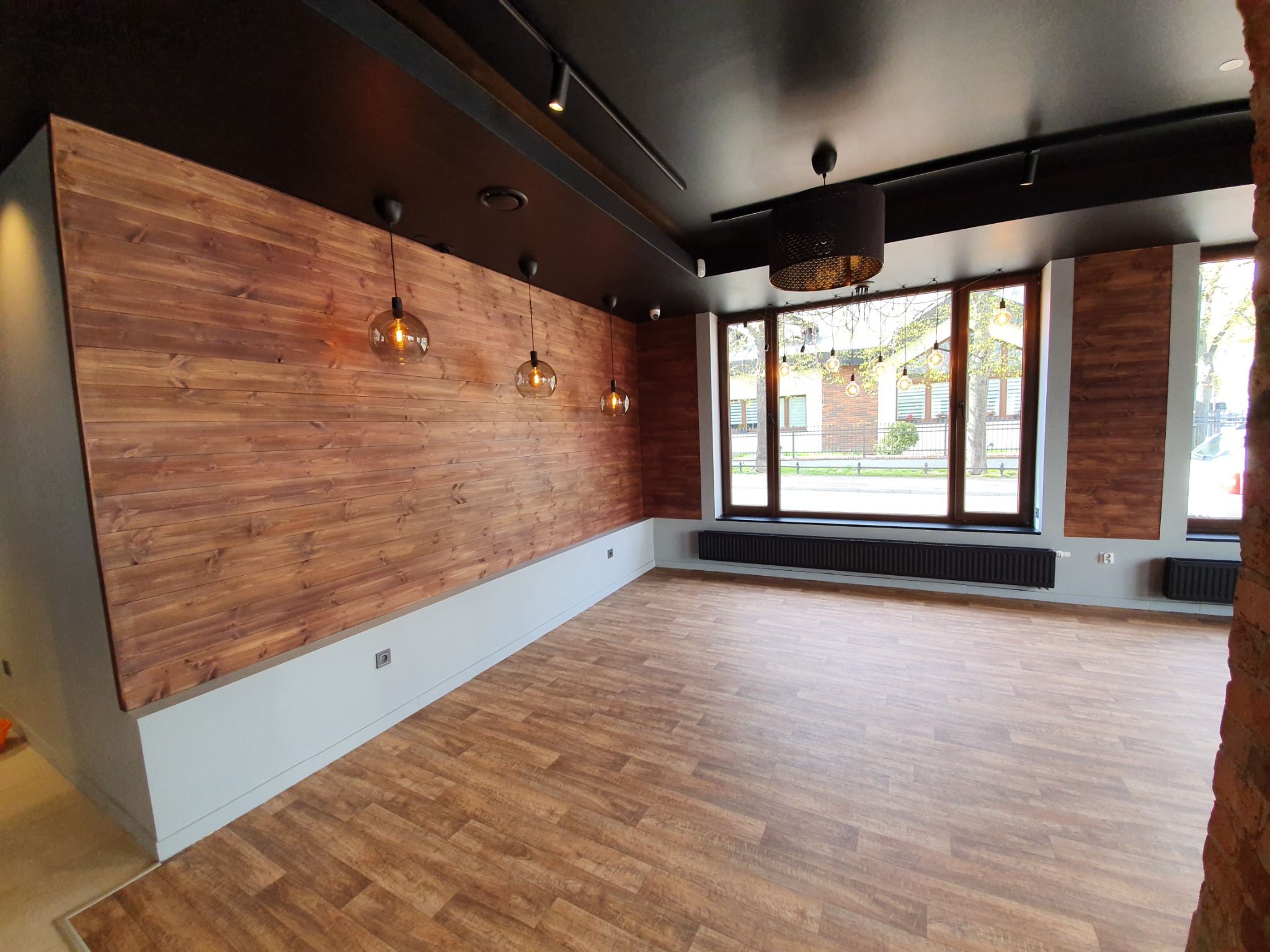 Wnętrze restauracji Endi Wine House w Sopocie: drewniana ściana z poziomych desek, podwieszane lampy z żarówkami Edisona, drewniana podłoga imitująca deski, czarny sufit z reflektorami szynowymi...