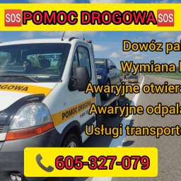 K.D Hol - Biała laweta z żółtym pasem i napisem 'POMOC DROGOWA' na poboczu autostrady, przewożąca uszkodzony, granatowy samochód osobowy.