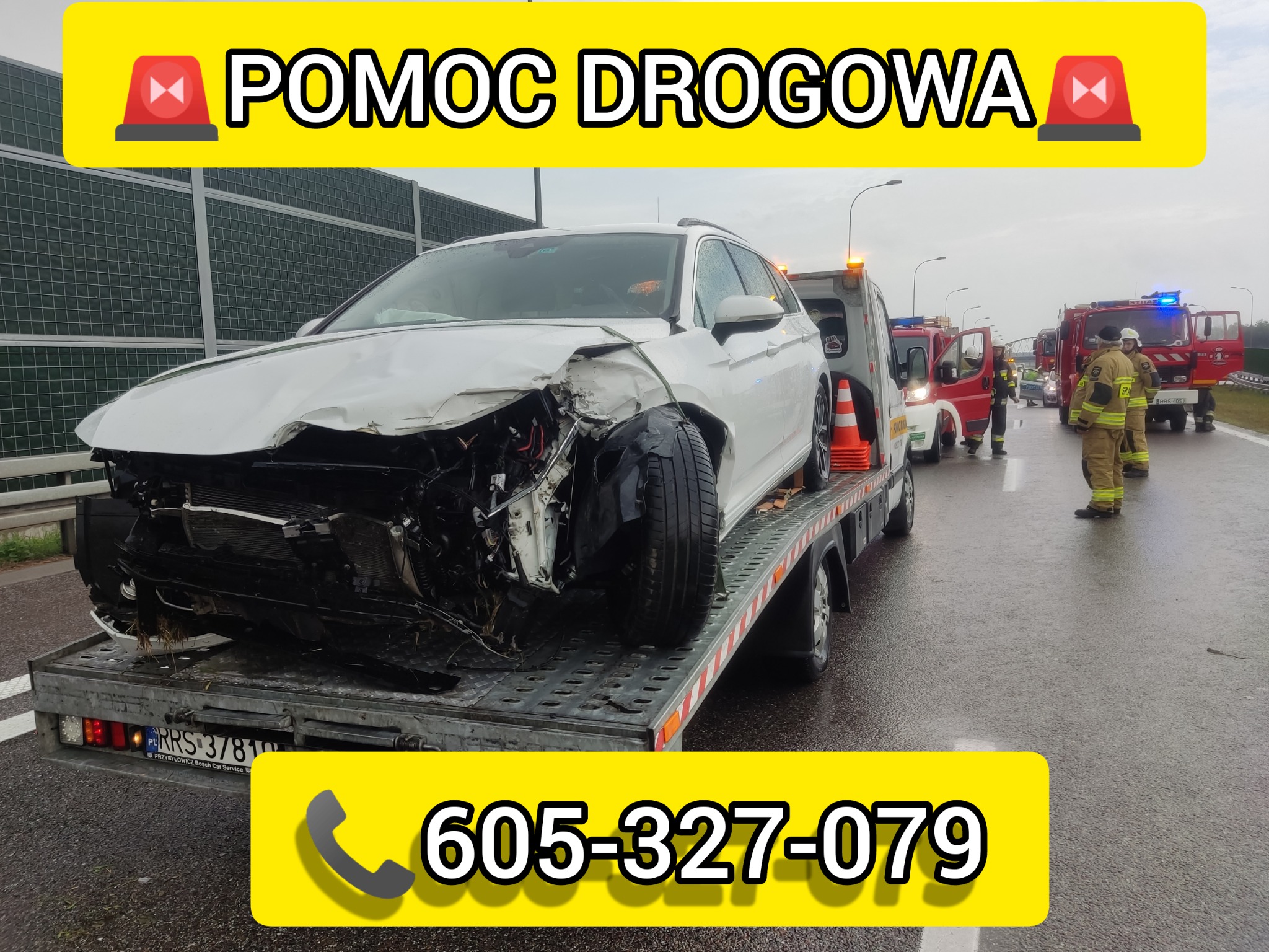 Uszkodzony biały samochód osobowy na platformie lawety po wypadku drogowym, na mokrej nawierzchni, w tle straż pożarna i ratownicy.