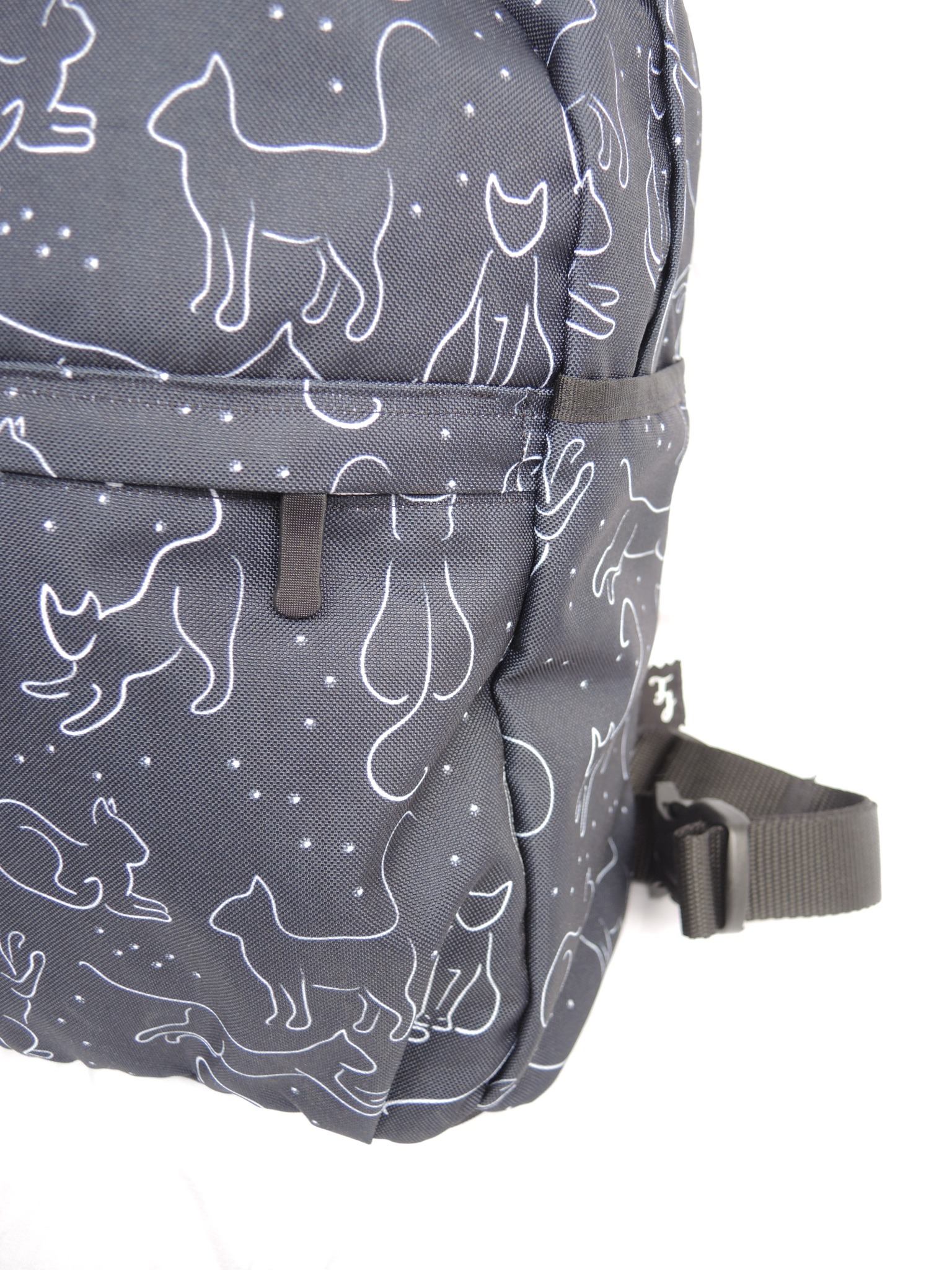 Fragment szarego plecaka z białymi konturami kotów i kropek, widoczny pasek i kieszeń z boku.