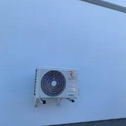 Biała jednostka zewnętrzna klimatyzacji Rotenso zamontowana na elewacji budynku z widocznym logo firmy.