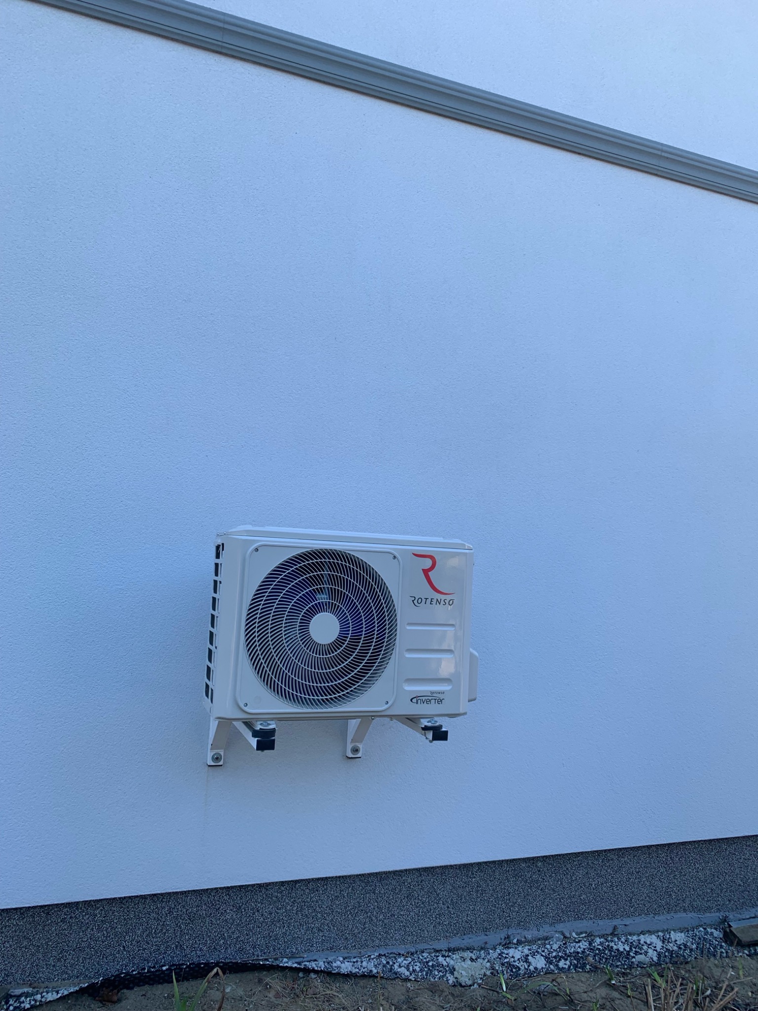 Biała jednostka zewnętrzna klimatyzacji Rotenso zamontowana na elewacji budynku z widocznym logo firmy.