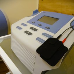 Warsztat Zdrowia - Aparat do elektroterapii z elektrodami na szklanym stoliku, widoczne przyciski sterujące i wyświetlacz.