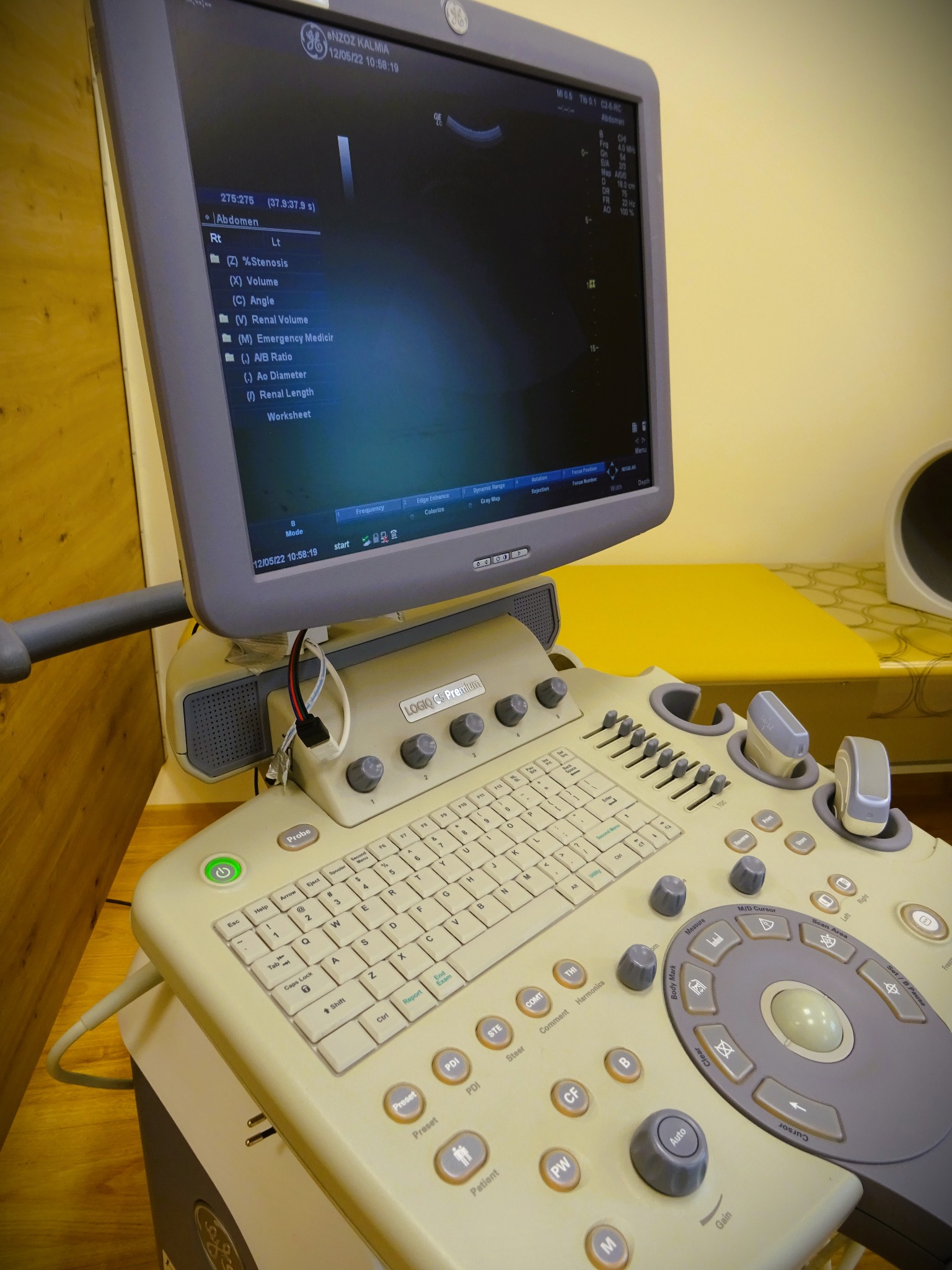 Aparat USG GE Logiq C5 Premium z widocznym ekranem wyświetlającym parametry badania jamy brzusznej, klawiatura i panel sterowania w kolorze beżowym.