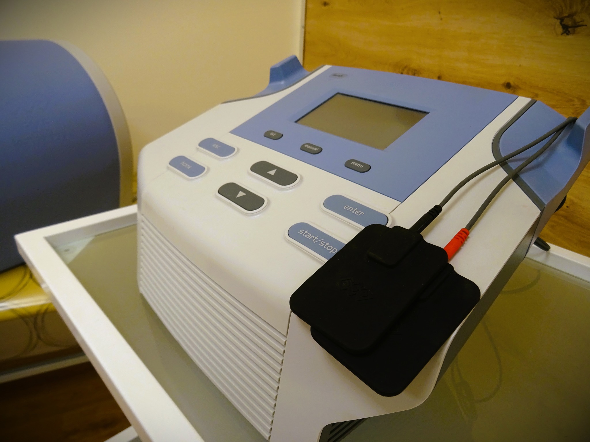 Aparat do elektroterapii z elektrodami na szklanym stoliku, widoczne przyciski sterujące i wyświetlacz.