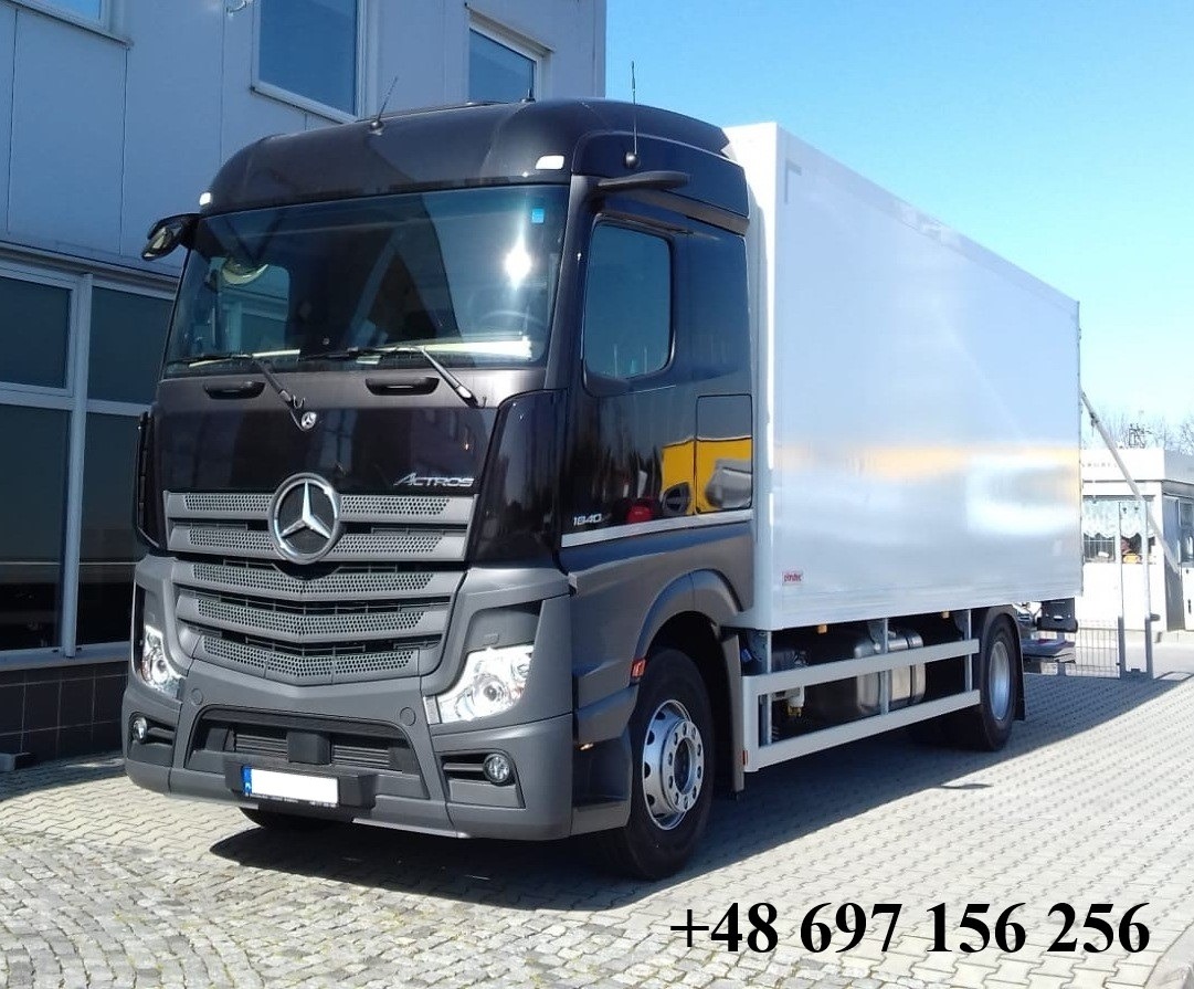 Czarno-szary samochód ciężarowy Mercedes Actros z białą zabudową kontenerową, zaparkowany na kostce brukowej. Widoczny numer telefonu na dole zdjęcia.