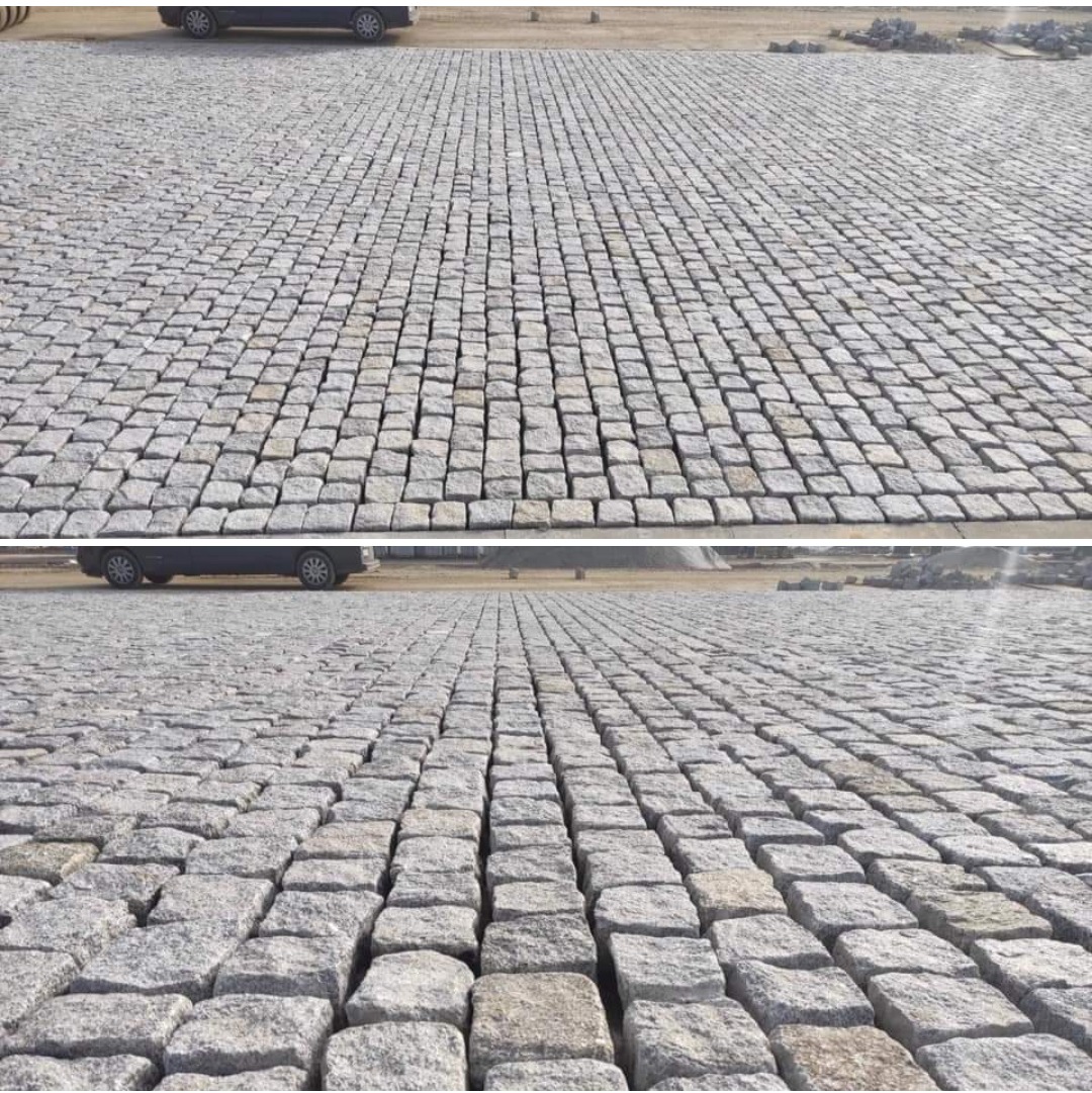 Rozległa powierzchnia wyłożona szarą kostką brukową, regularny wzór z widocznymi fugami, samochód w tle, ujęcie z dwóch perspektyw.