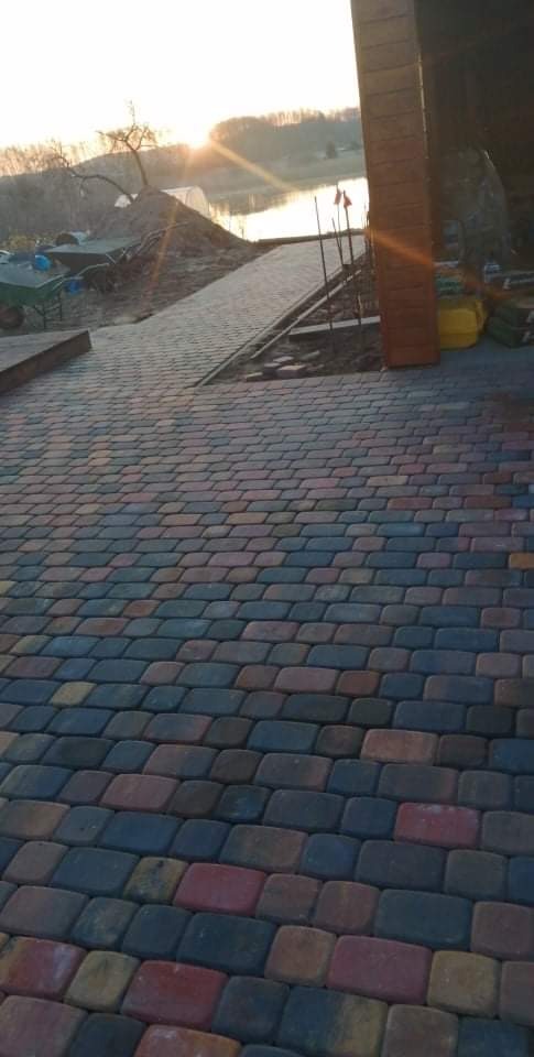 Kolorowa kostka brukowa ułożona w Złotowie, prowadząca w kierunku jeziora w promieniach zachodzącego słońca. Na drugim planie widoczna sterta ziemi i taczka.