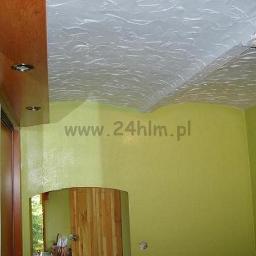 Remonty, wykończenia wnętrz Szczecin, 24 HLM - Żółto-zielona ściana z lustrem i drewnianą szafą wnękową, sufit z fakturą imitującą fale, widoczny fragment lampy. Na ścianie widoczny adres strony internetowej.